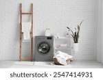 Interior of laundry room with grey washing machine, laundry basket and ladder