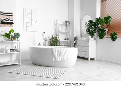 Interior of light bathroom with bathtub and Monstera houseplant - Shutterstock ID 2297491043
