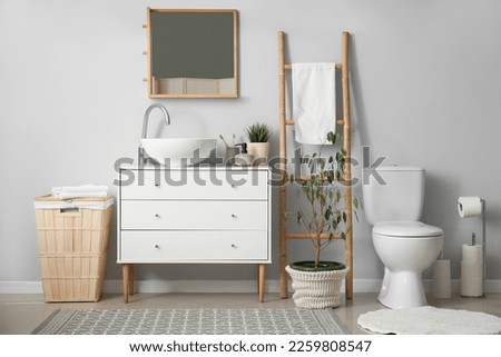 Interior of light bathroom with drawers, toilet bowl and laundry basket
