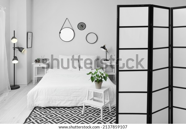 Interior of light bedroom with folding screen and\
glowing lamp