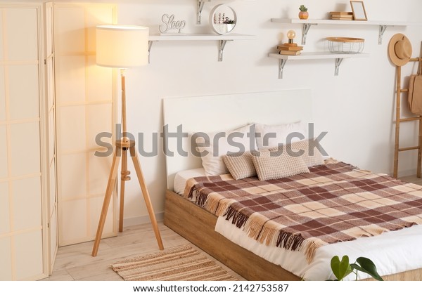 Interior of light bedroom with folding screen and\
glowing lamp