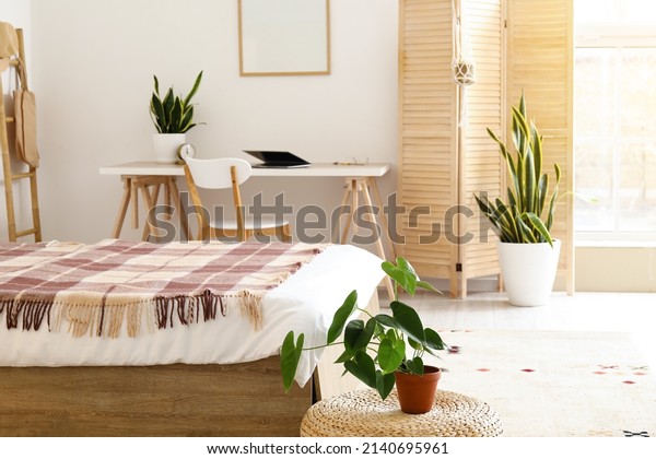 Interior of light bedroom with wooden folding\
screen and modern\
workplace