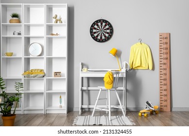 Interior of light children's room with workplace, shelving unit and dartboard