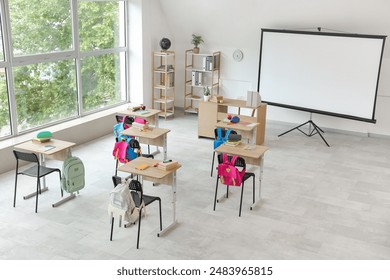 Interior of light classroom with projector screen and desks