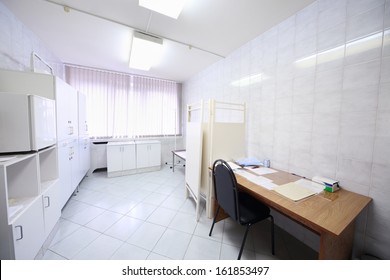 Interior of a light doctors consulting room with table, cabinet and folding screen