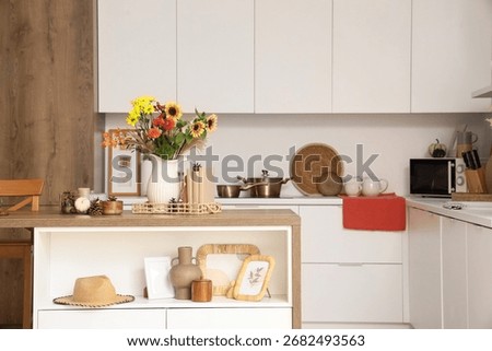 Interior of light kitchen with table, counters and autumn flowers in vase