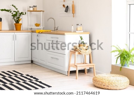 Interior of light kitchen with white counters and wooden step stool