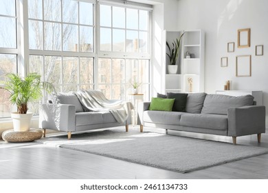 Interior of light living room with cozy grey sofas near big window