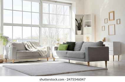 Interior of light living room with cozy grey sofas near big window