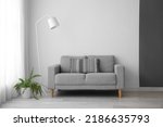 Interior of light living room with grey sofa, standard lamp and houseplant