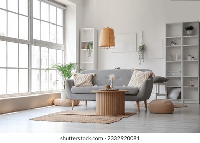 Interior of light living room with grey sofa, wooden coffee table and big window