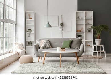 Interior de sala de estar luminosa con sofá gris, mesa baja y gran ventana