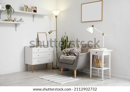 Interior of light living room with lamps, armchair and commode