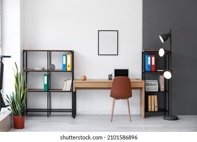 Interior Of Light Office With Workplace, Shelving Units And Glowing Lamp