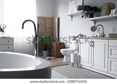 Interior of light restroom with ceramic toilet bowl, sink and vanity cabinets