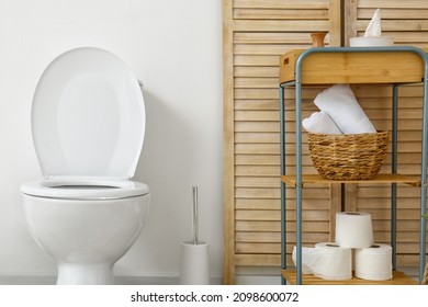 Interior of light restroom with toilet bowl and shelving unit