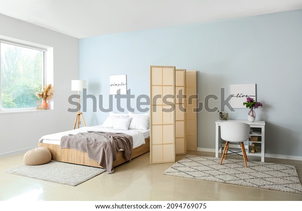 Interior of light room with bed, folding screen\
and modern workplace