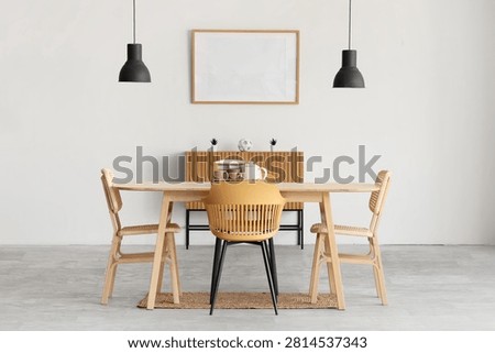 Interior of light room with blank frame, commode and dining table