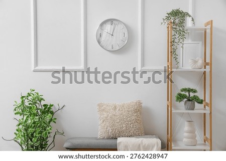 Interior of light room with wall clock, soft bench and shelf unit