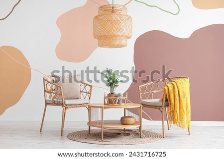 Interior of living room with armchairs, cushion and houseplant near spotty wall