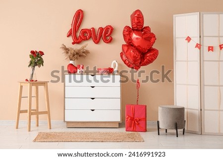 Interior of living room with chest of drawers and decorations for Valentine's Day celebration near beige wall