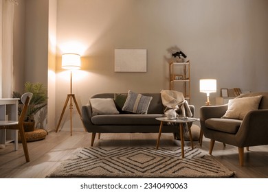 Interior of living room with cozy grey sofa, armchair and glowing lamps - Shutterstock ID 2340490063