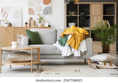 Interior of living room with dirty clothes on sofa
