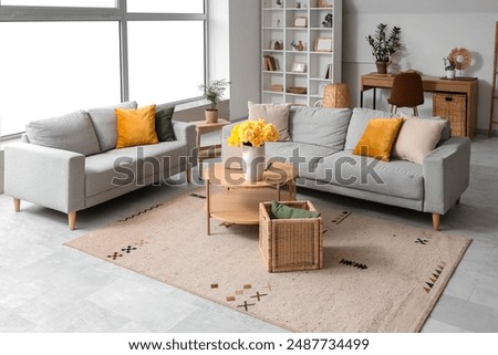 Interior of living room with grey sofas, laptop and yellow narcissus flowers on wooden coffee table