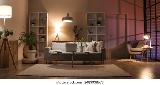 Interior of living room with sofa, armchair, table and glowing lamps in evening