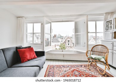 Interior Of Living Room With White Wall Furnished With Sofa And Rattan Chair On Persian Rug With Windows Viewing Old Town