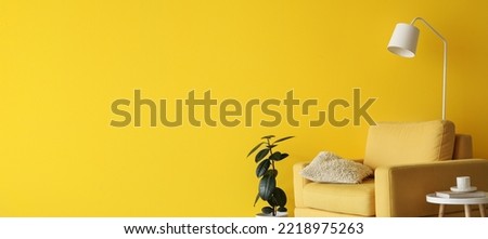 Interior of living room with yellow armchair, table, houseplant and lamp near yellow wall with space for text