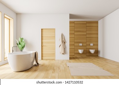 Interior Of Loft Bathroom With White Walls, Wooden Floor And White Bathtub With Towel On It Standing Under Windows. Door In The Wall And Two Toilets. 3d Rendering