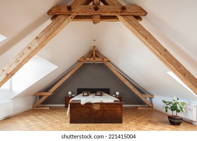 Interior of a loft or dormer bedroom in the apex of a roof with visible timber roof trusses , a patterned parquet floor and double bed