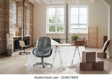 Interior Of Loft Space With Furniture Covered With Polyethylene And Many Cardboard Boxes, Moving Into New Office Concept