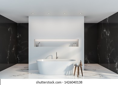 Interior Of Luxury Bathroom With Black Marble And White Walls, White Marble Floor, White Bathtub With Shelf Above It And Small Chair With Towels And Shampoos. 3d Rendering