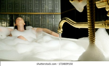 Interior of a luxury bathroom. Close up of a vintage bathtub faucet with a young woman taking a bath on a blurred background.