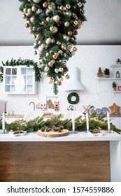 Interior of minimalistic kitchen with white walls, white floor, white countertops. Kitchen with white furniture. Kitchen decorated with  garlands and Christmas toys. Christmas tree upside down.
