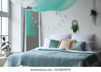 Interior of modern bedroom with bed, mirror and dream catcher hanging on light wall