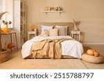 Interior of modern bedroom with comfortable bed, bedside table and pumpkins on ottoman