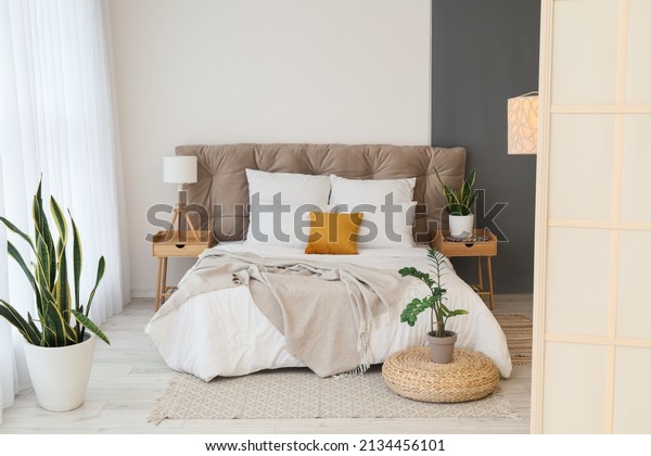 Interior of modern bedroom with stylish\
folding screen, nightstands and\
houseplants