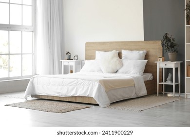 Interior of modern bedroom with white bed and alarm clock on bedside table