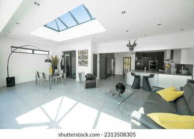 Interior of modern, bright, white and grey designer open plan kitchen diner and lounge, with skylight roof lantern.