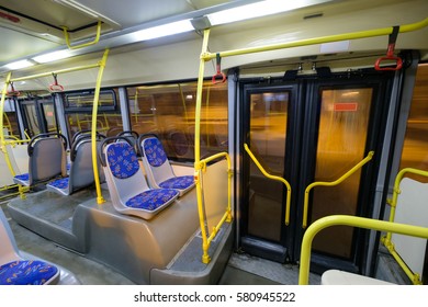 Interior Of Modern City Bus With Seats, Doors And Handles In Night. Wide Angle Shot Form Back Side