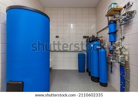 The interior of a modern gas boiler room with a blue tank and cylinders and various equipment. Water purification sistem