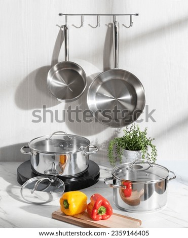 interior of a modern kitchen with cooking equipment for preparing healthy meals, stainless steel hanging pans, pots, and peppers on a white marble countertop
