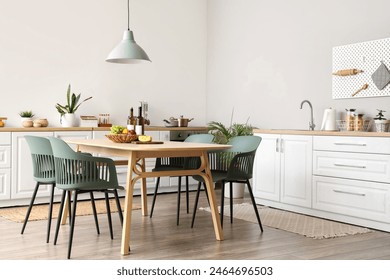 Interior of modern kitchen with dining table, chairs, white counters and lamp