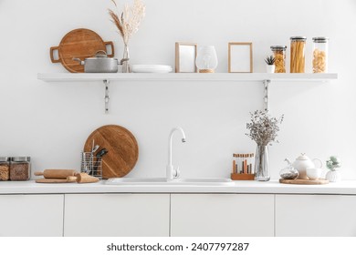 Interior of modern kitchen with white counters, shelf, sink and utensils