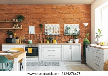 Interior of modern kitchen with white counters, pegboard and brick wall