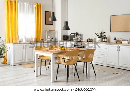 Interior of modern kitchen with white counters, dining table, yellow curtains, chairs and lamp