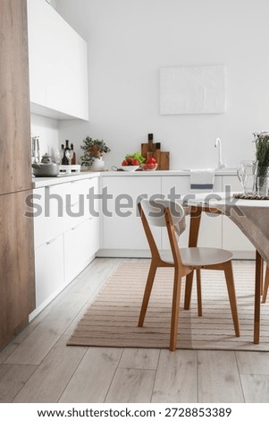 Interior of modern kitchen with white counters, dining table and stylish rug